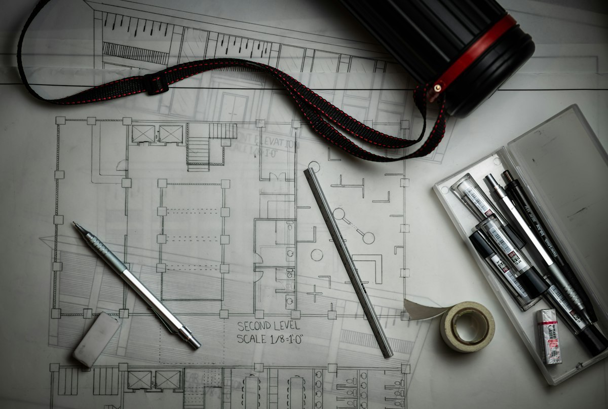 Architectural blueprints with pencils, a metal ruler and a drawing-storage tube