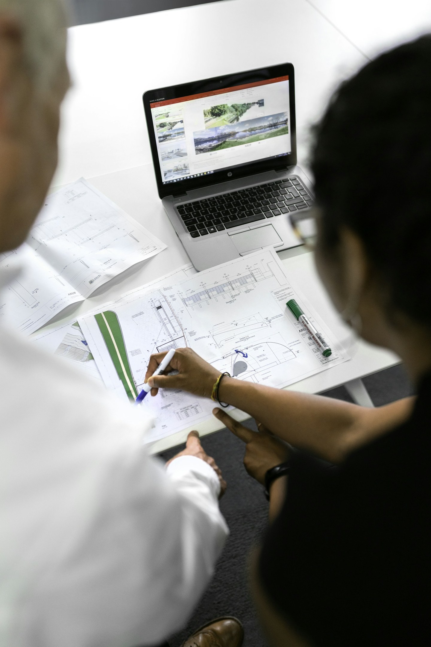Close overhead view of a civil engineer annotating flood management drawings next to a laptop