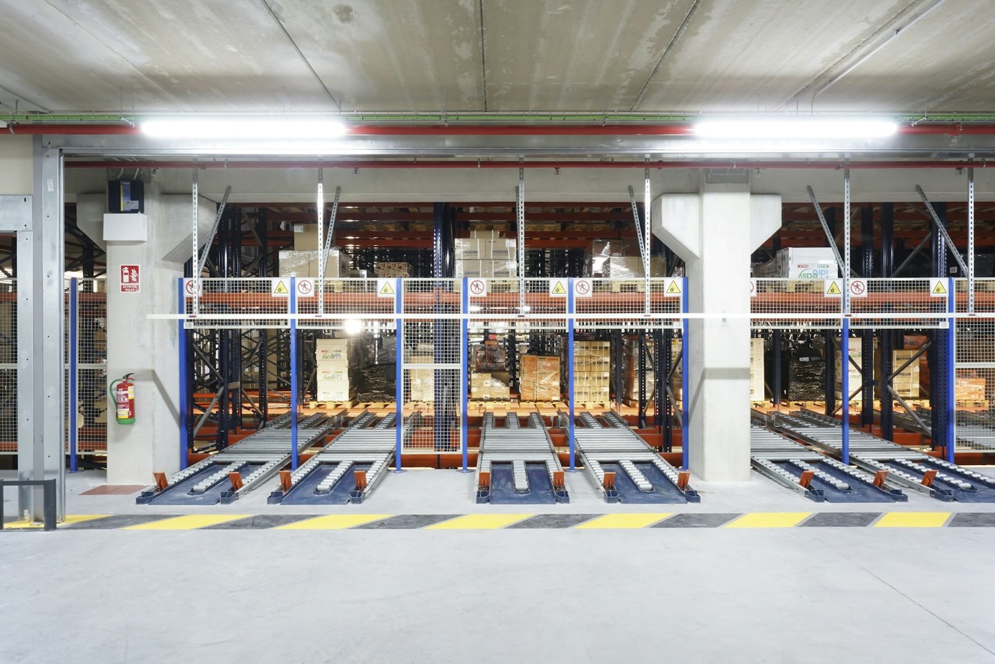 Pallets stored in an industrial rack system behind conveyor lanes and safety fencing