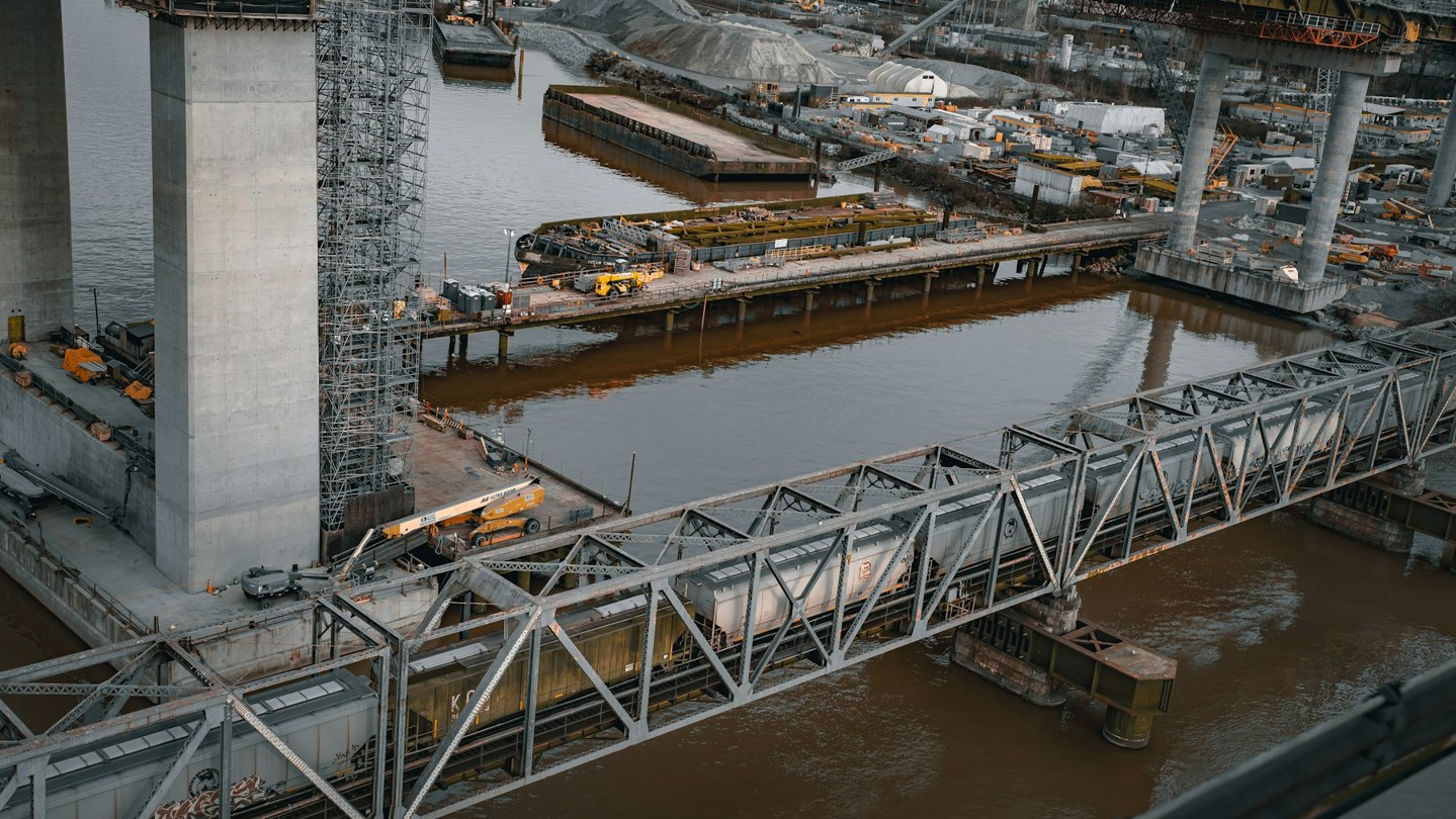 Cranes, temporary works and bridge piers beside a railway bridge over water in New Westminster