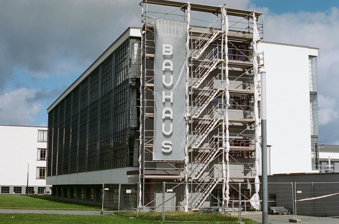 Scaffolding alongside the glass facade and Bauhaus sign of an educational building undergoing renovation