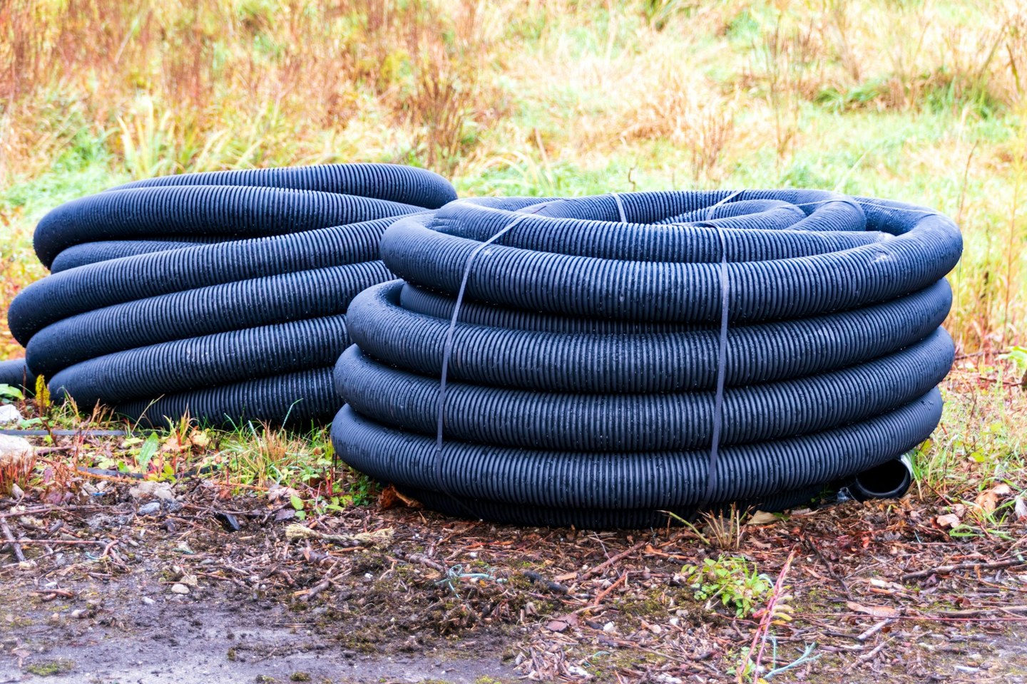 Two large coils of black corrugated drainage pipe stored on the ground