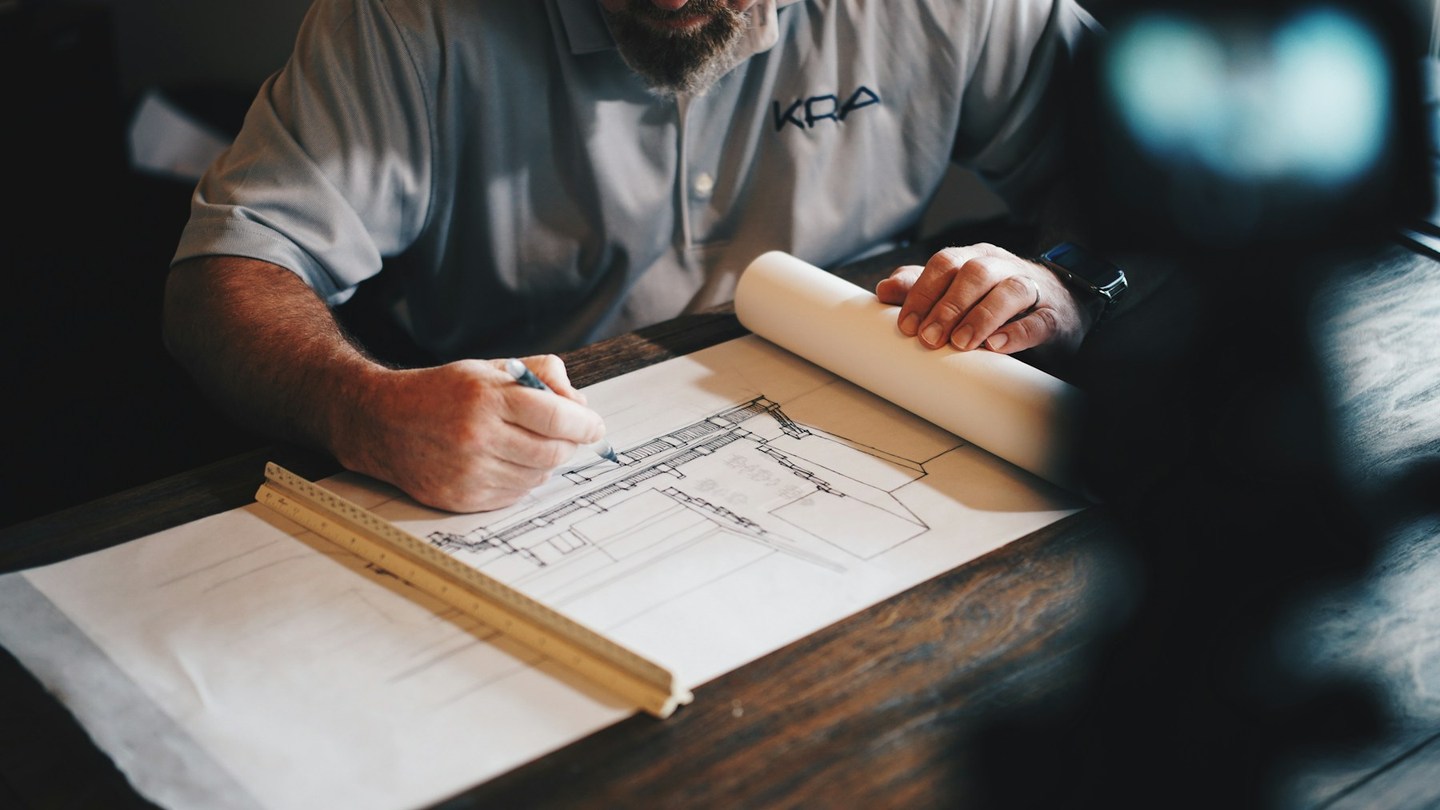 Hands using a pencil and scale ruler on a large architectural drawing