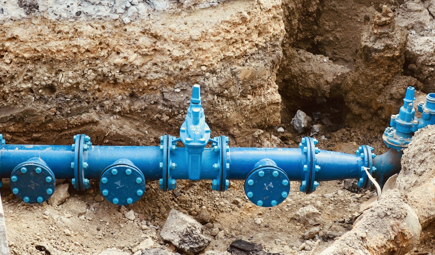 Blue flanged utility pipe and valves exposed in an excavated trench